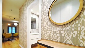 A modern bathroom with a round mirror, patterned wallpaper, and a wooden vanity. - Apt. 1 br. Cathedral I, Historic Center (Valladolid)