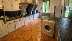 Une cuisine avec des meubles blancs, un lave-linge et un sol carrelé.