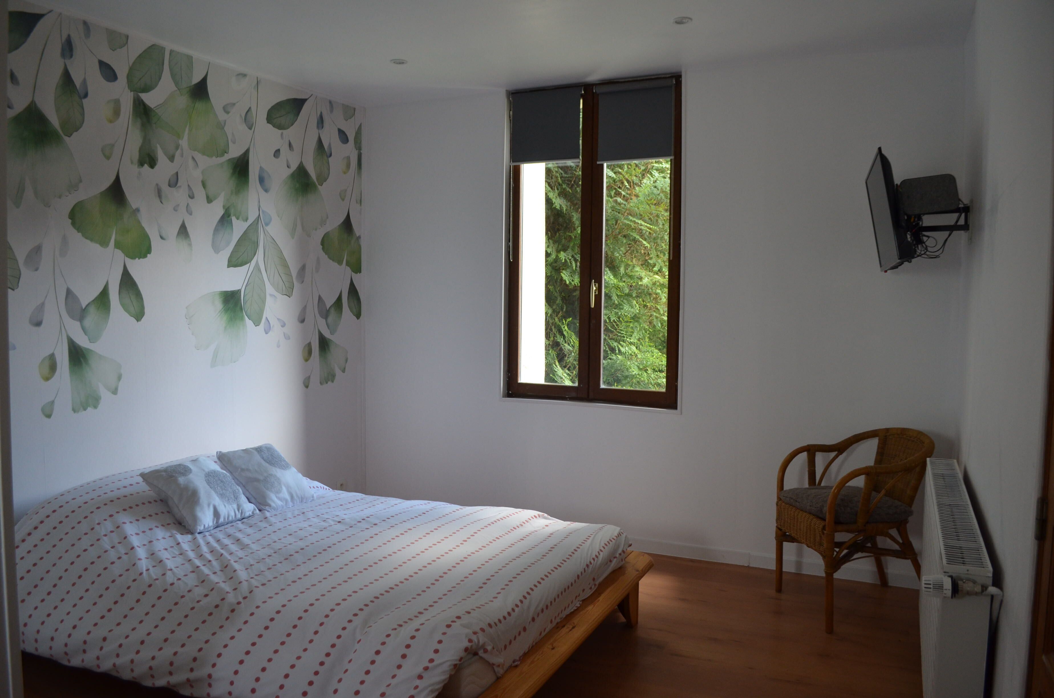 A bedroom with a bed, a chair, a radiator, and a window with a view of greenery.