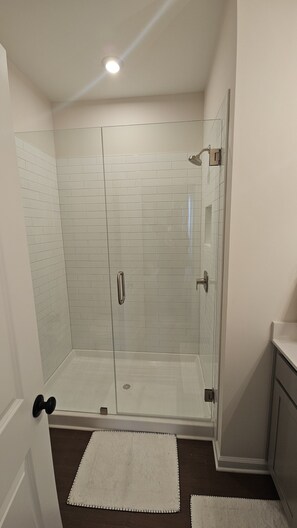 A glass-enclosed shower with white tiled walls and a ceiling light. - Modern Cozy Retreat in Prime Location (Atlanta)