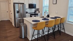 Een moderne keuken met een centraal eiland, barkrukken en een koelkast van roestvrij staal.