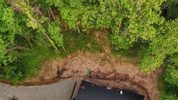 Une vue aérienne d’un bâtiment entouré d’une forêt dense, avec un chemin de gravier menant à l’entrée.