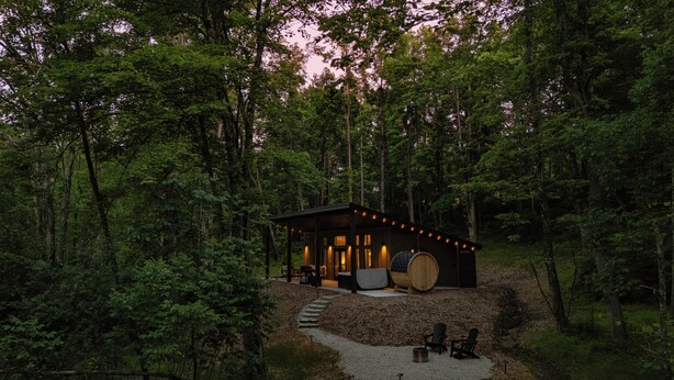 A cabin surrounded by dense forest, with a stone staircase leading up to the entrance. - Modern Couples Cabin - Hot Tub + Outdoor Shower (Logan)