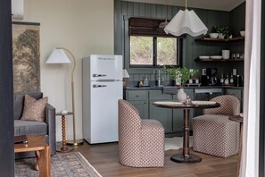 Eine kompakte Küche mit Kühlschrank, Esstisch, zwei Stühlen, einer Couch und einer Lampe.