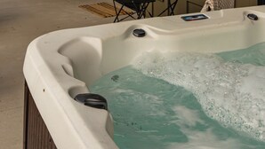 A hot tub with a wooden deck, outdoor seating, and large windows. - Modern Couples Cabin - Hot Tub + Outdoor Shower (Logan)