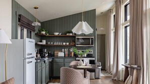 A modern kitchen with a dining area, a refrigerator, microwave, and a hanging light fixture. - Modern Couples Cabin - Hot Tub + Outdoor Shower (Logan)