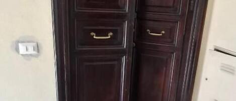 Una porta doppia in legno scuro con maniglie dorate, una parete di colore chiaro e un pavimento piastrellato.