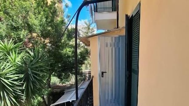 Un balcone con pavimento piastrellato, ringhiera in metallo e una porta con finestra.