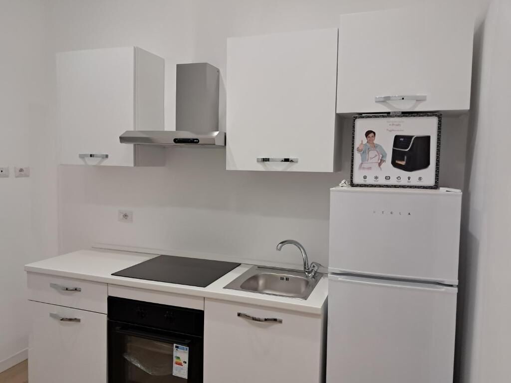 A modern kitchen with white cabinetry, a built-in oven, a sink, and a refrigerator.