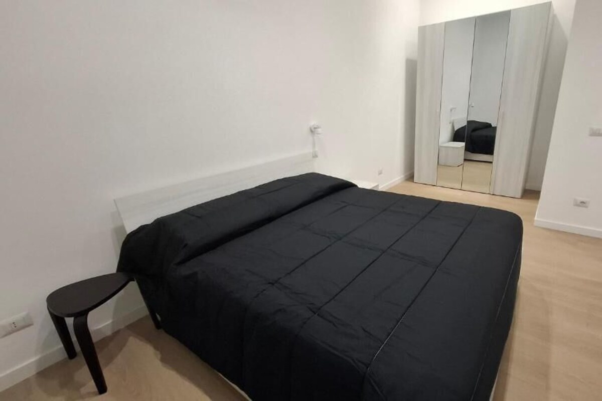 A bedroom with a bed, a small table, a wardrobe, and a mirror.