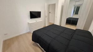 Una camera da letto con un letto, una TV su un mobile, una porta e uno specchio che riflette l'ambiente.