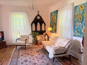 Una sala de estar con sofá, sillón, televisor, candelabro, pinturas y un icono religioso.