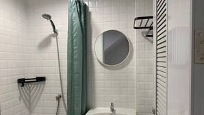 A bathroom with white tiled walls, a green shower curtain, a round mirror, a white sink, and a towel rack. - Room-charming B&B Retreat in Vibrant Phr (Bangkok)