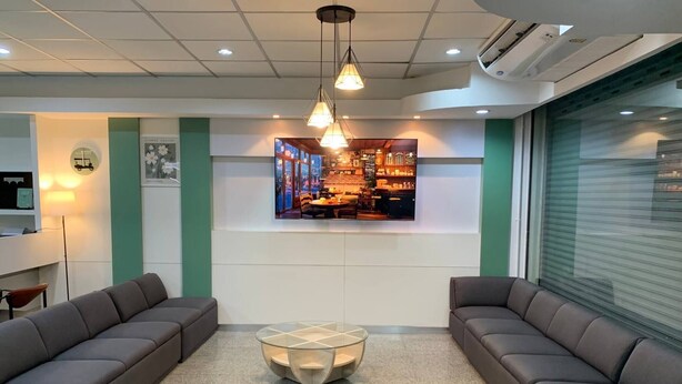 A modern lobby with seating areas, a central glass table, and a wall-mounted TV displaying a bar scene. - Room-charming B&B Retreat in Vibrant Phr (Bangkok)