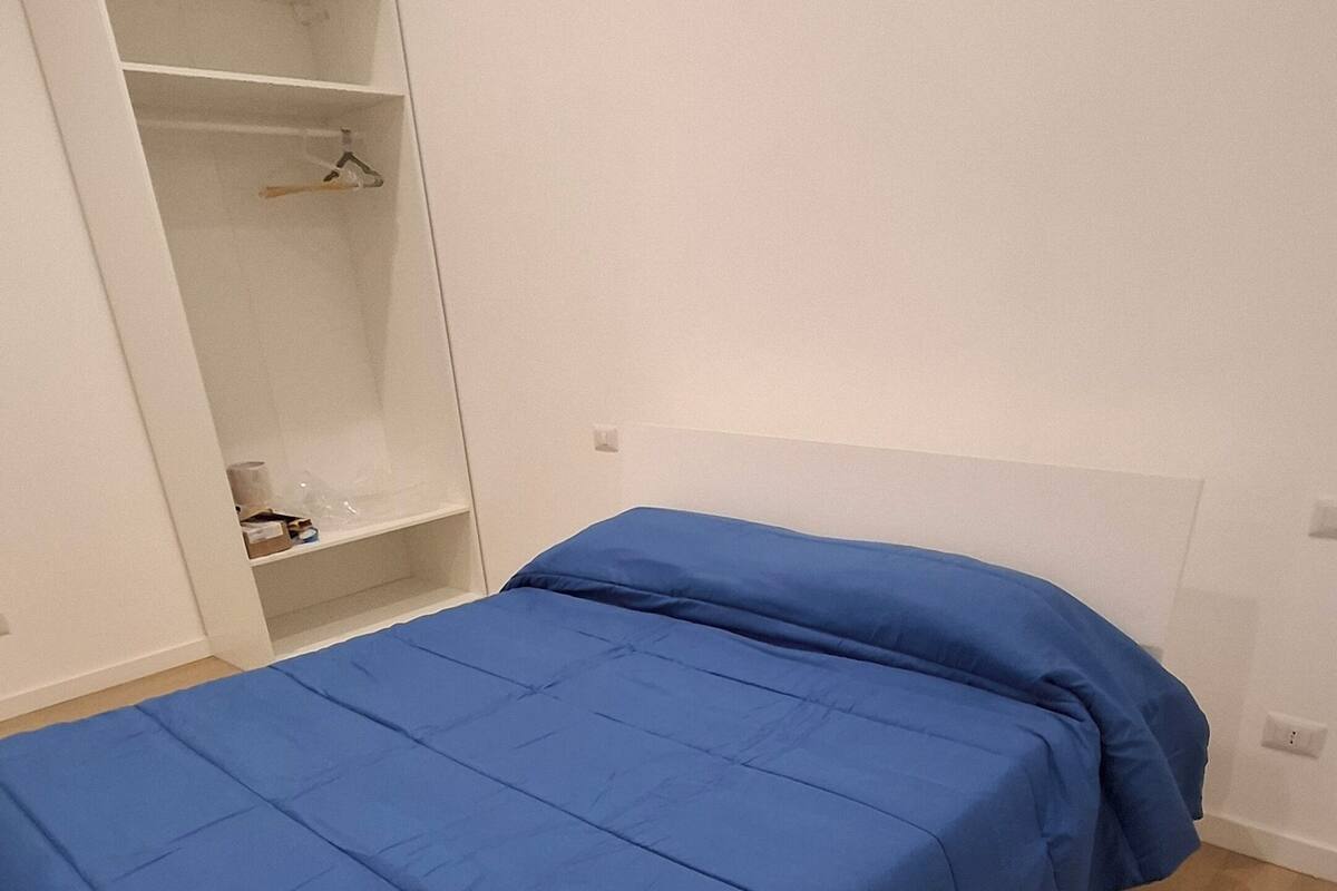 A single bed with a blue bedspread in a room with white walls and a wooden floor.