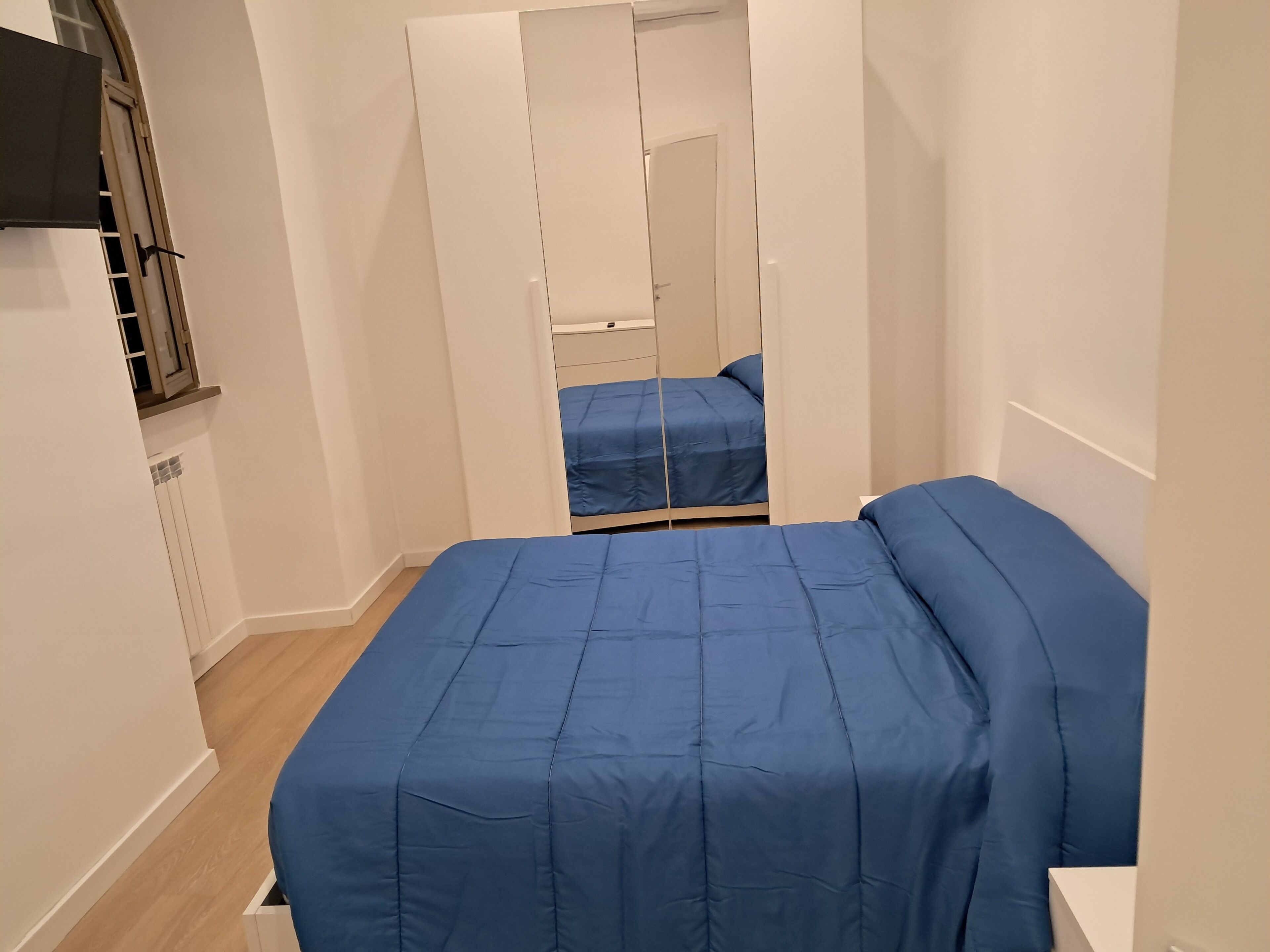 Una habitación pequeña con cama, espejo y ventana.