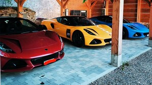 Ett överbyggt parkeringsområde med tre sportbilar parkerade under en träkonstruktion.