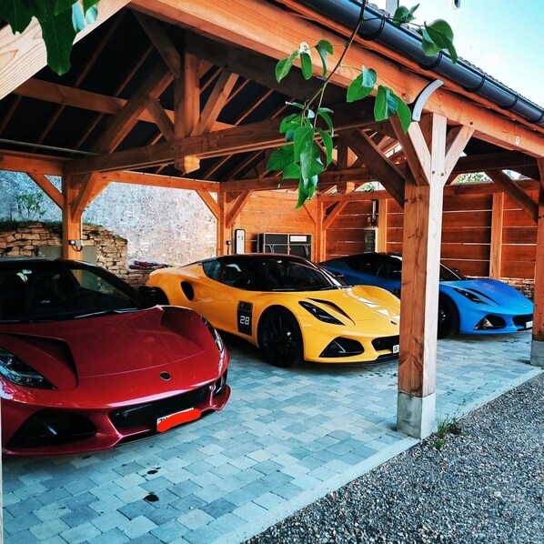 A covered parking area with three sports cars parked under a wooden structure. - FORMOSA Dijon (Étaules)