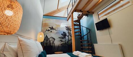 A bedroom with a bed, pillows, a wall mural, a staircase, a TV, and a skylight.
