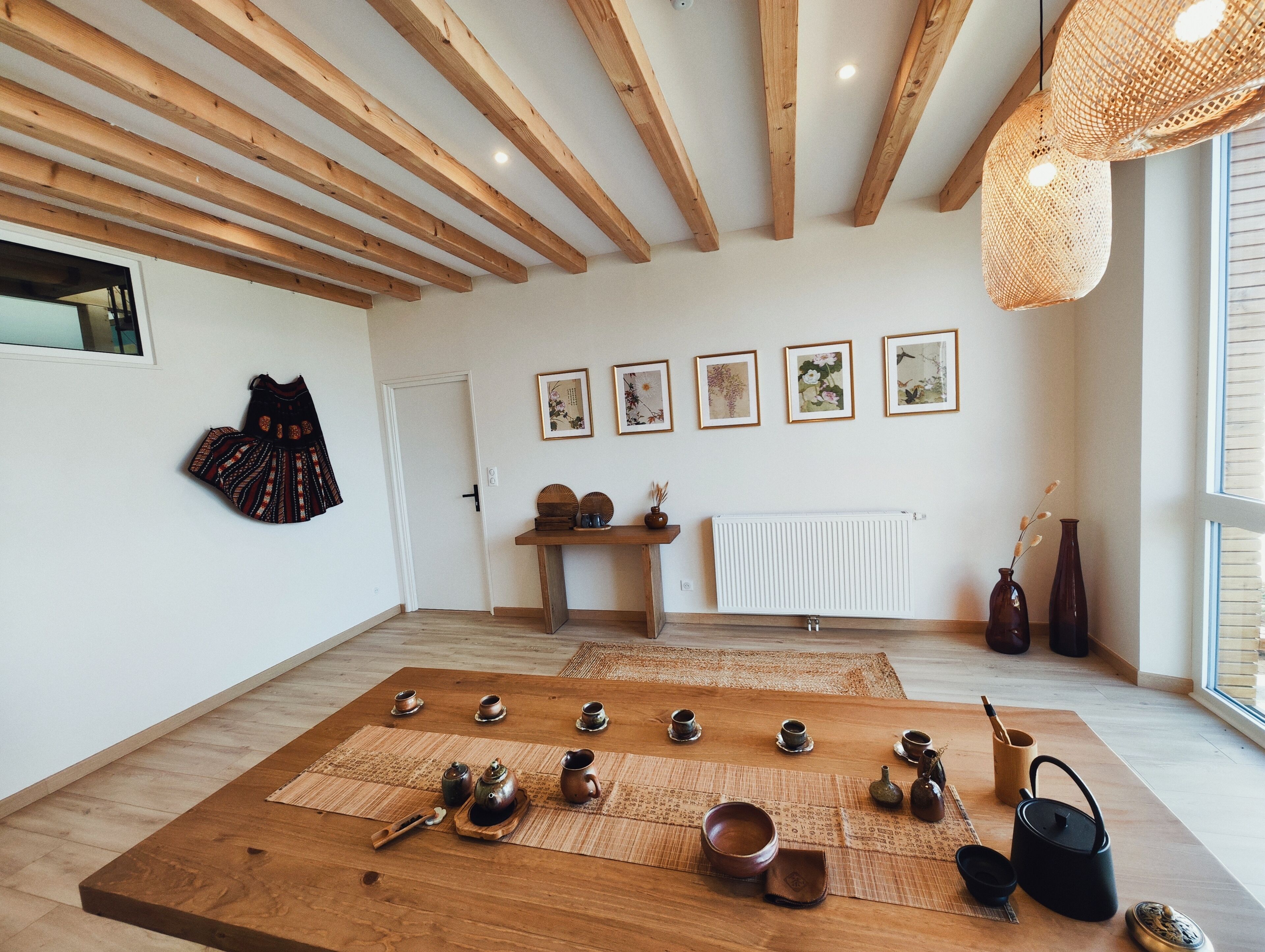 A room with wooden beams, a tatami mat, a tea set, and framed artwork on the wall.