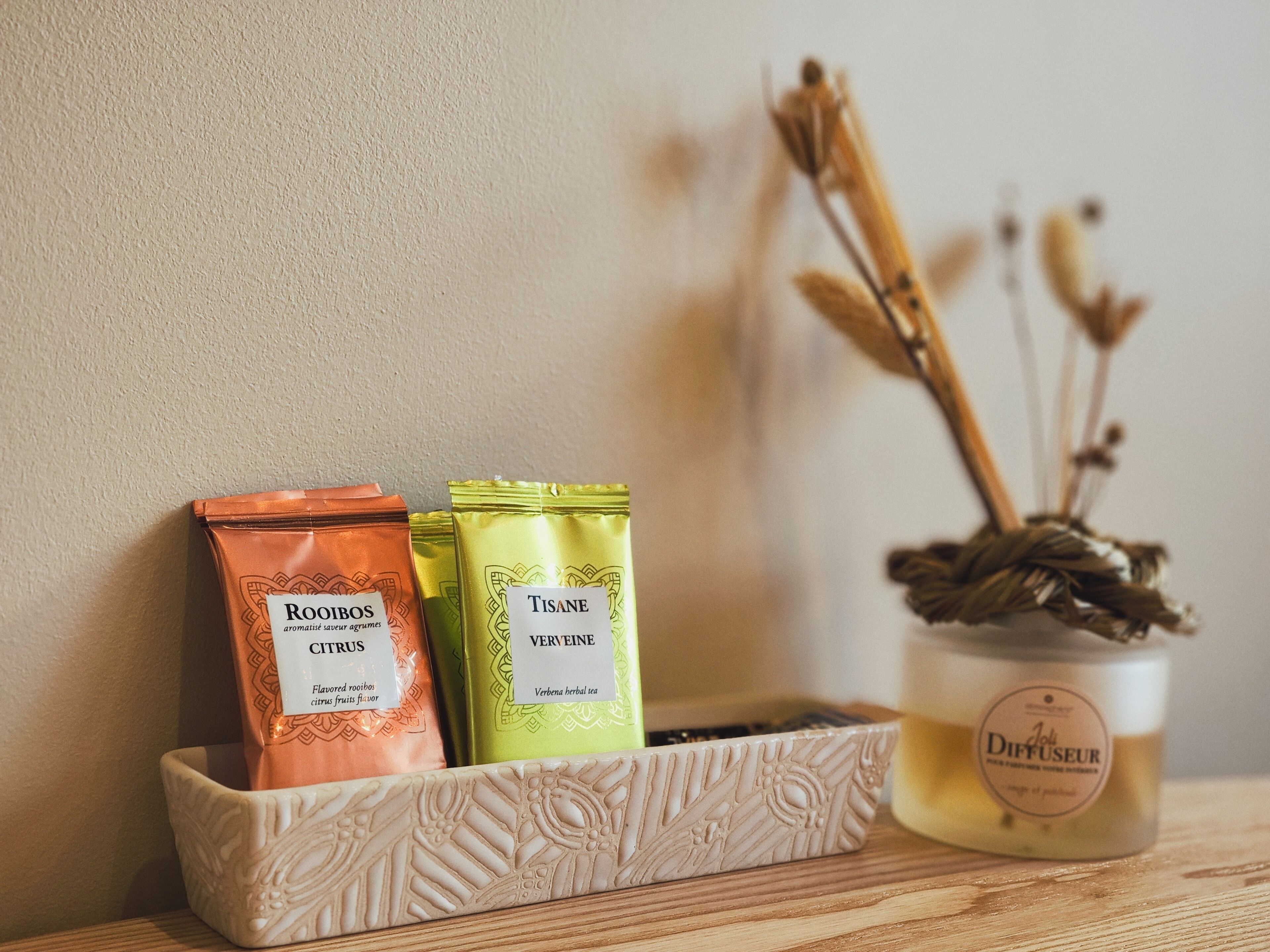 A tray with three bags of herbal tea and a diffuser on a wooden surface.