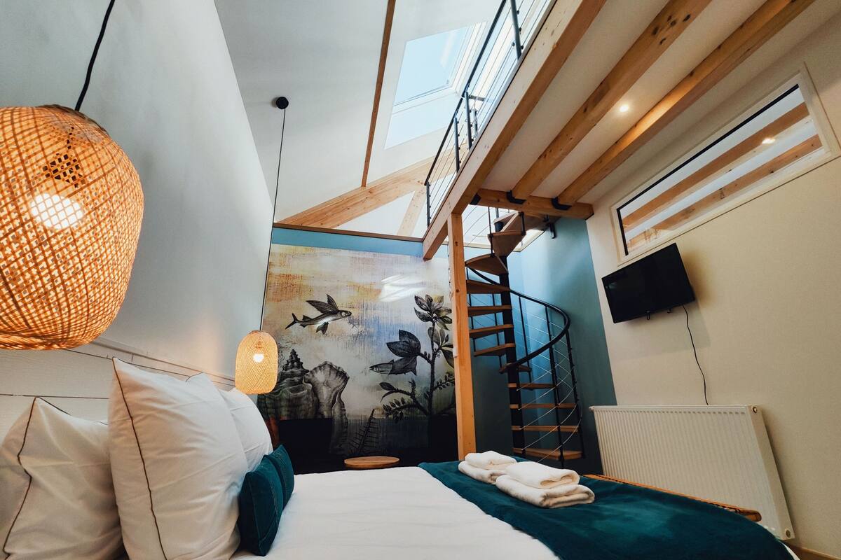 A bedroom with a bed, a wall mural, a staircase, and a skylight.