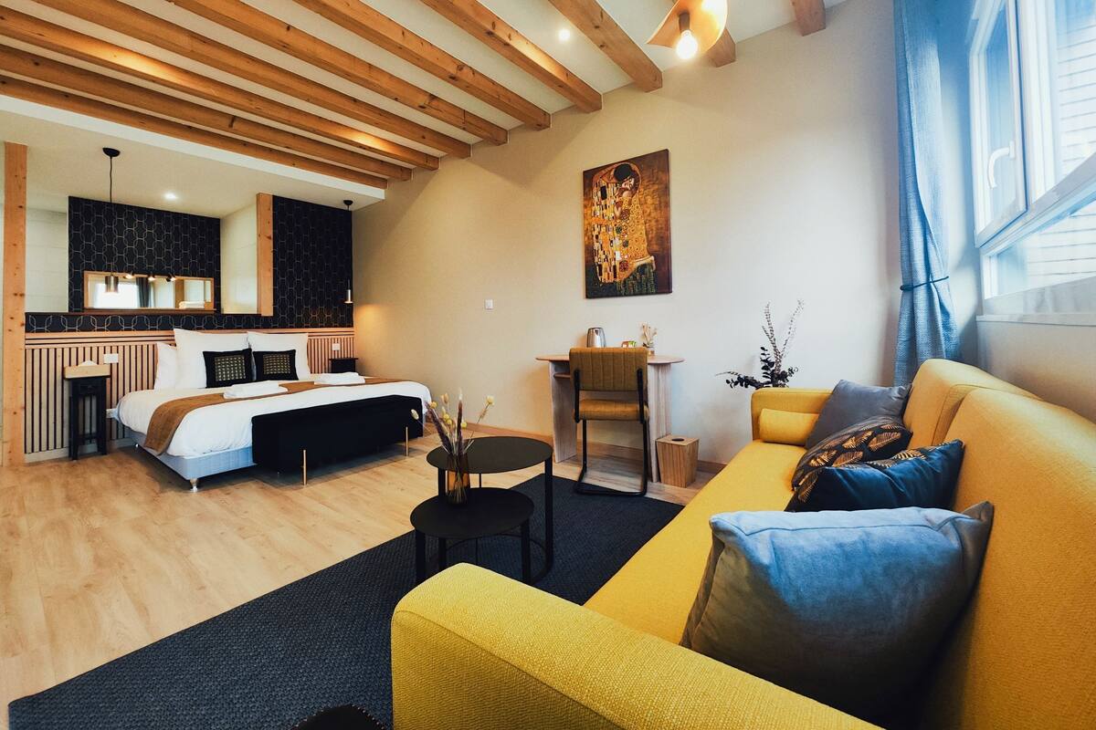A modern hotel room with a bed, a sofa, a dining area, and a kitchen.