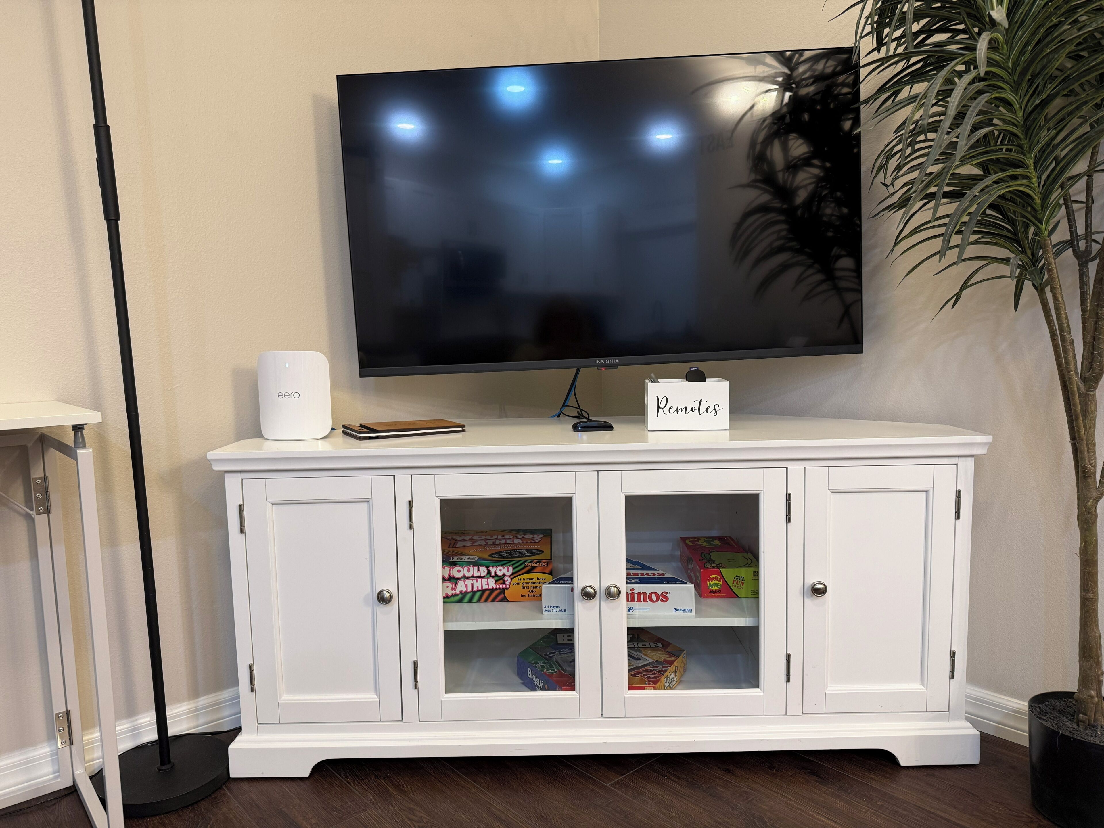 Un televisor de pantalla plana montado en un mueble blanco con puertas de vidrio, un control remoto y un cartel en el mueble que dice 'Mandos a distancia'.