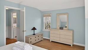 Quarto com cama, cômoda, espelho e janela.