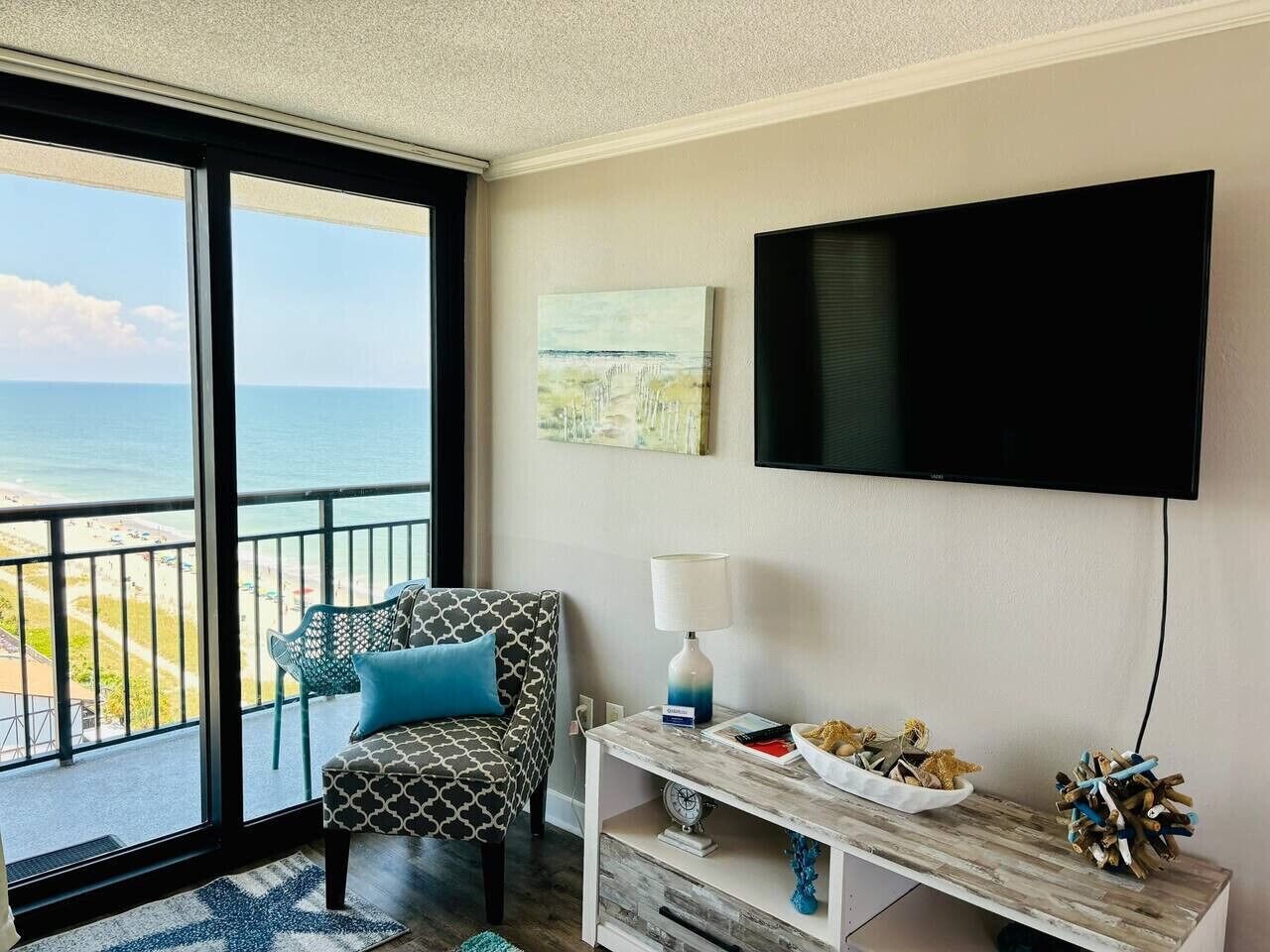 A room with a view of the ocean, a sofa with a patterned cushion, a television, and a small table with decorative items.
