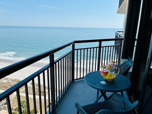 Un balcon avec vue sur l’océan, une table ronde avec des chaises et une boisson posée sur la table.