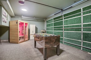 Une pièce avec un baby-foot, un meuble en bois, une armoire blanche et un mur recouvert de gazon synthétique vert.