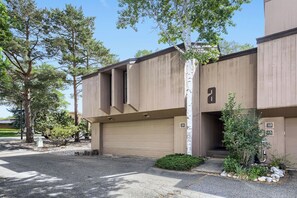 A modern two-story building with a garage, a small front yard with a tree, and a clear sky.