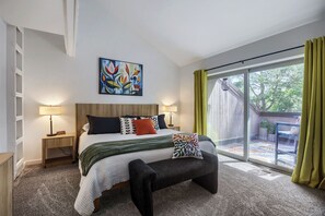 A bedroom with a bed, bedside tables, a bench, a painting, and a view of an outdoor area.