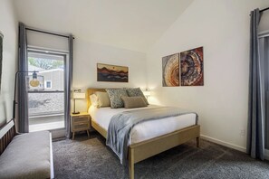 A bedroom with a bed, bedside tables, a window, and artwork on the walls.