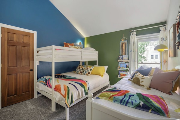 Une chambre avec des lits superposés, une porte en bois, une bibliothèque et une fenêtre donnant sur un paysage agréable.