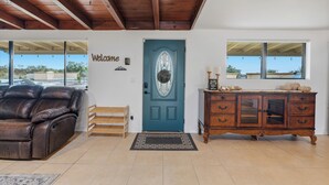 Una sala de estar con un sofá de cuero, una puerta azul, un mueble de madera y vistas amplias a través de ventanas grandes.