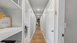Un pasillo con puertas blancas, suelo de madera y una estantería con una cita enmarcada.