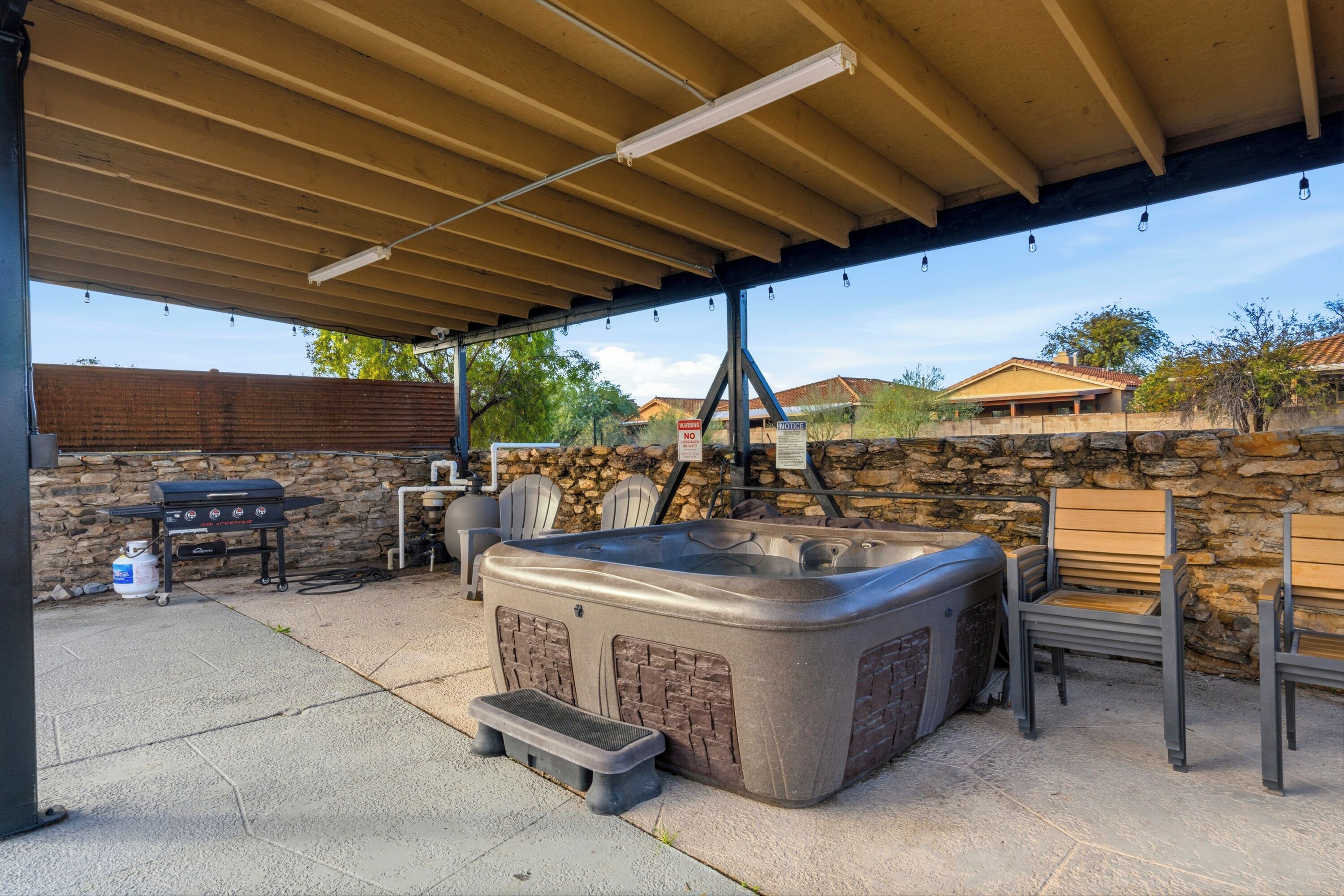 A covered outdoor patio with a hot tub, barbecue grill, and seating area.