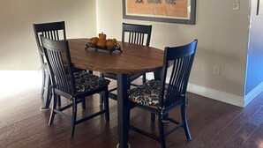 A dining area with a wooden table, four chairs, a ceiling fan, and a framed artwork on the wall.