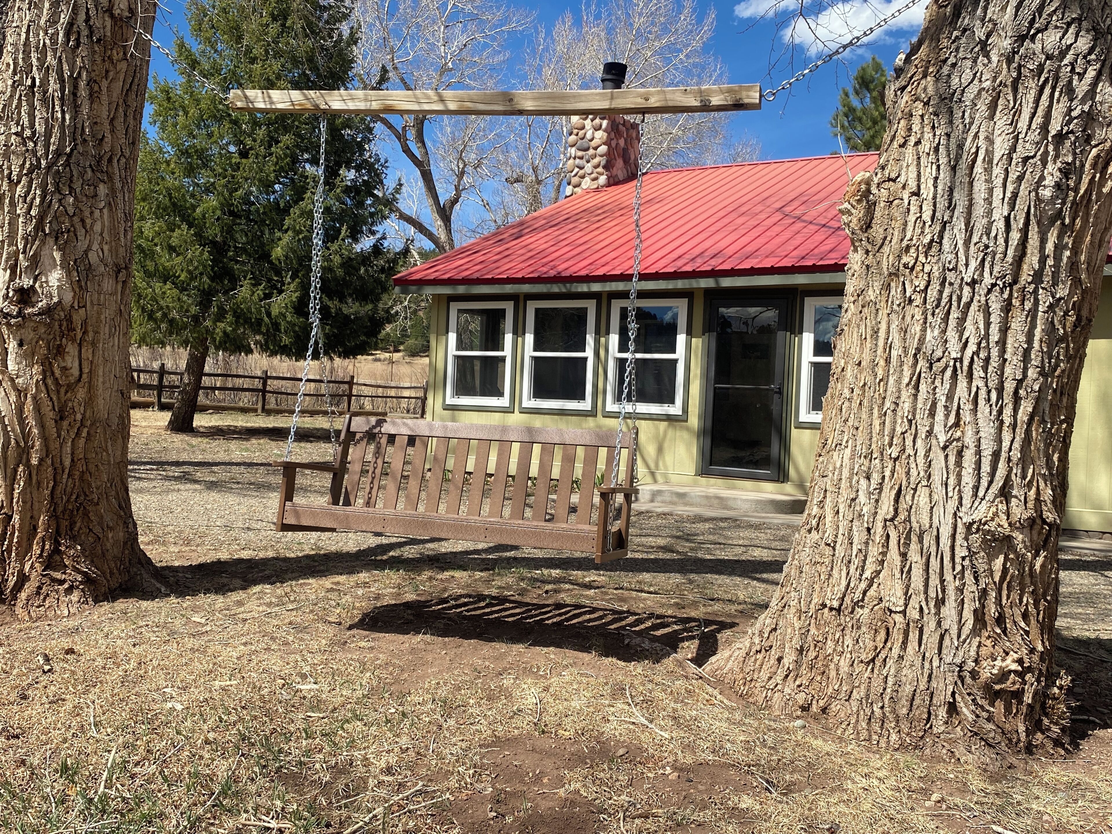 A wooden swing attached to a metal frame, a bench, and a building with a red roof and windows.