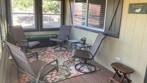 A covered porch with a seating area, including a bench and chairs, a small table with a plant, and a wooden stool.