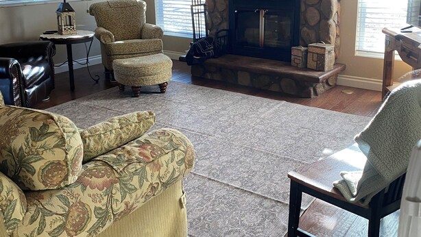 A living room with a stone fireplace, patterned sofas, a wooden ceiling, and a view through the windows.