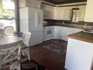 A kitchen with white cabinets, a refrigerator, an oven, and a dining area with a table and chairs.