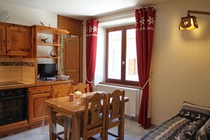 A kitchen with wooden cabinets, a dining table with chairs, a window with curtains, and a radiator. - Apartment Sabot de Venus (Val-Cenis)