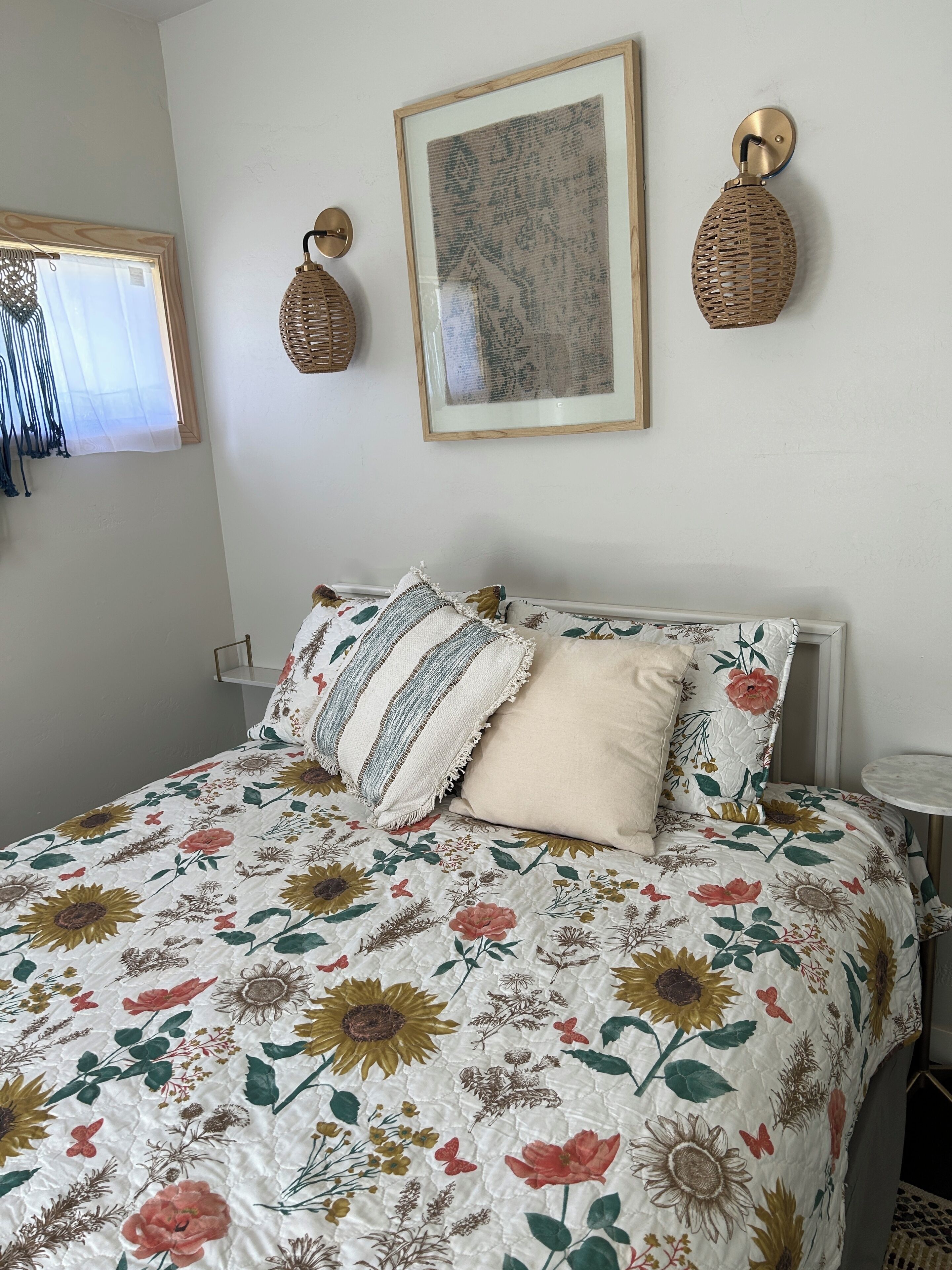 Een bed met een quilt met bloemenprint, een ingelijst schilderij en twee wandlampen.