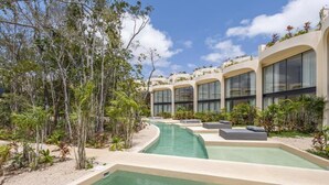 Un área de piscina con varias piscinas, zonas de descanso y un edificio con grandes ventanales.