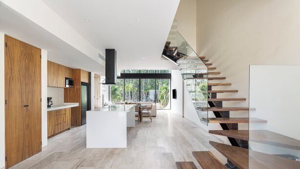 Una cocina moderna con armarios de madera, una isla central y una escalera de cristal.