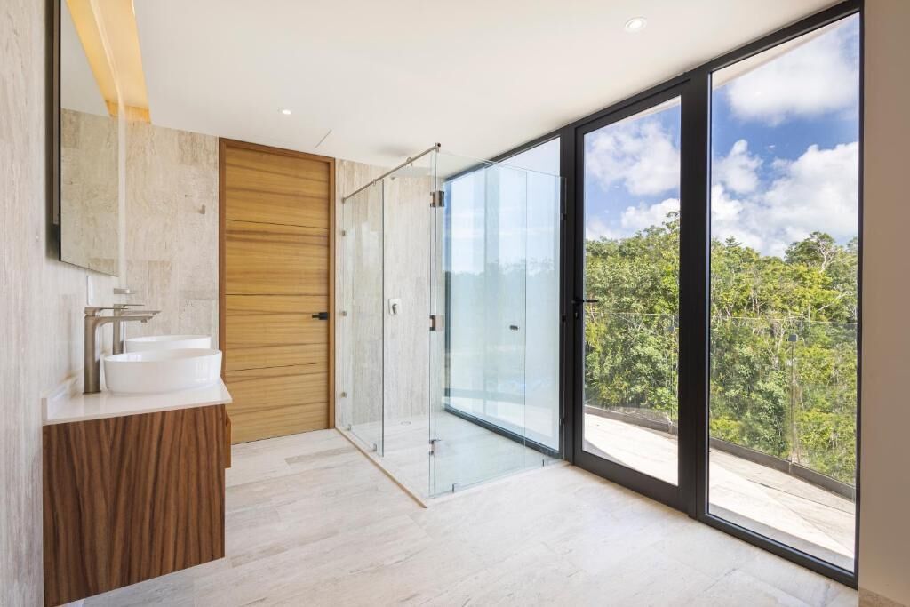 A modern bathroom with a large window, a wooden door, and a glass shower enclosure.
