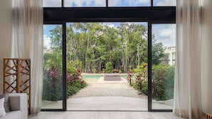 Una habitación moderna con un amplio ventanal corredera que da a un jardín con piscina y vegetación.